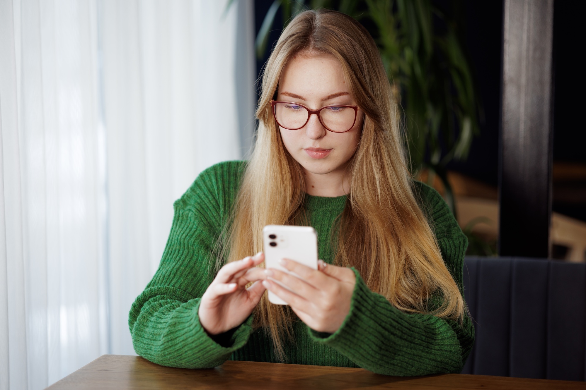 a young girl writes a message on the phone while sitting at the table, working online, chatting
