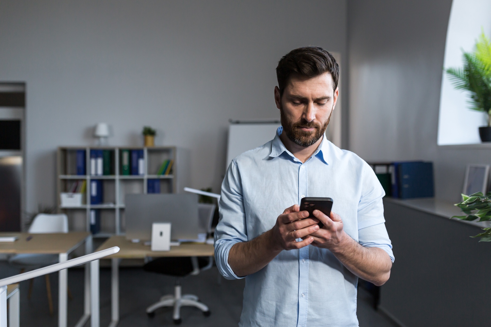 Portrait of a young man in the office. Stands, uses the phone, writes a message