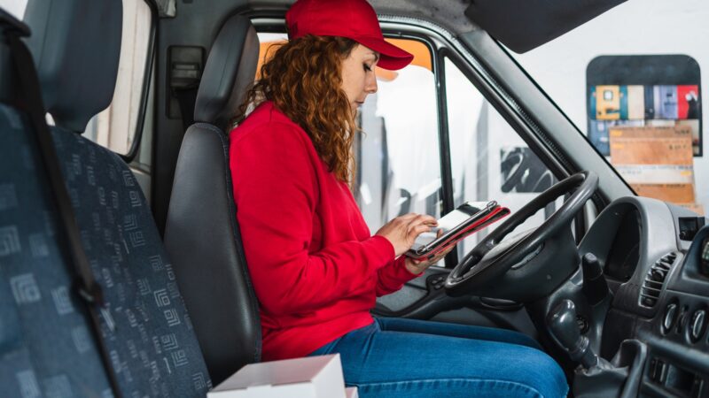 Female delivery driver tracking packages on a tablet in the car