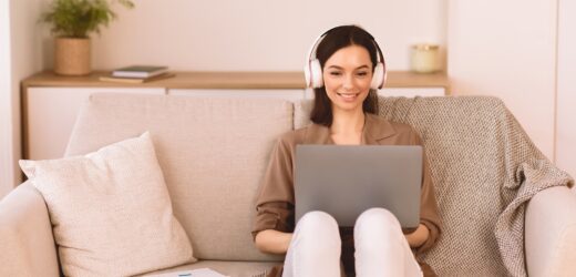 Girl listening to music online in headphone sitting on sofa