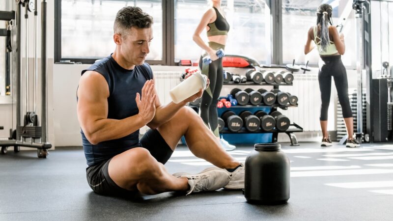 Strong man making protein cocktail in gym