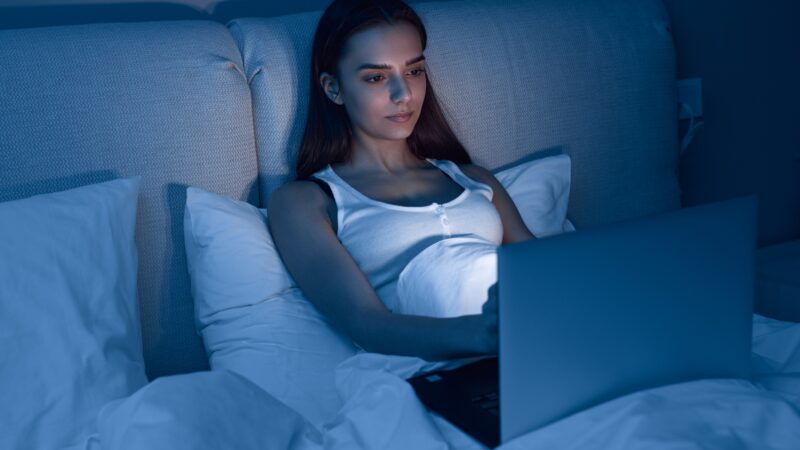 Young woman using laptop in bed at night