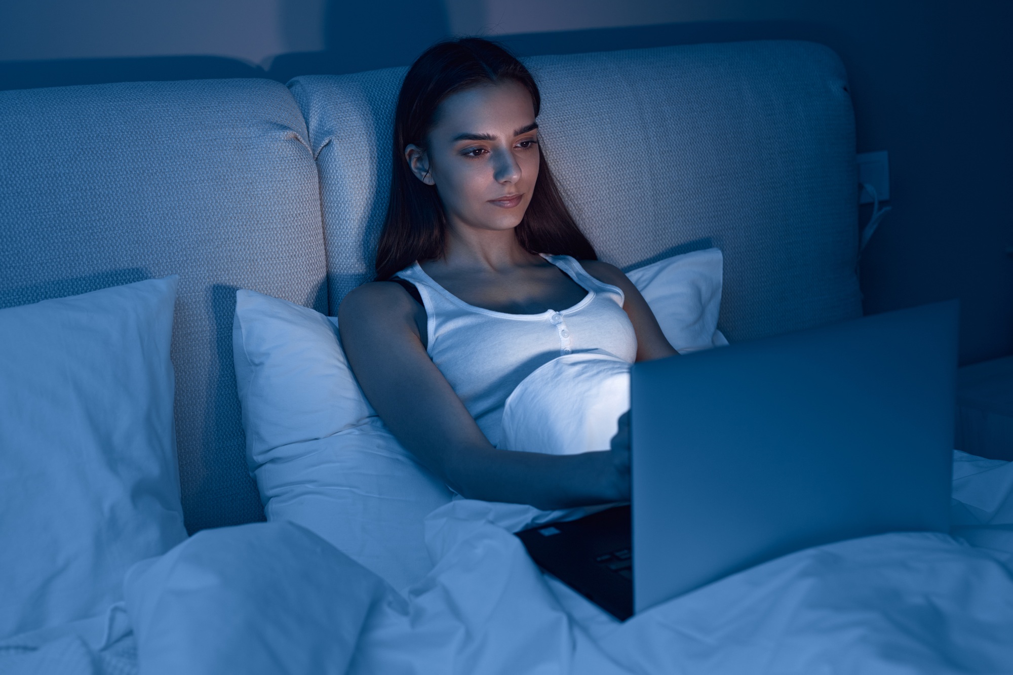 Young woman using laptop in bed at night